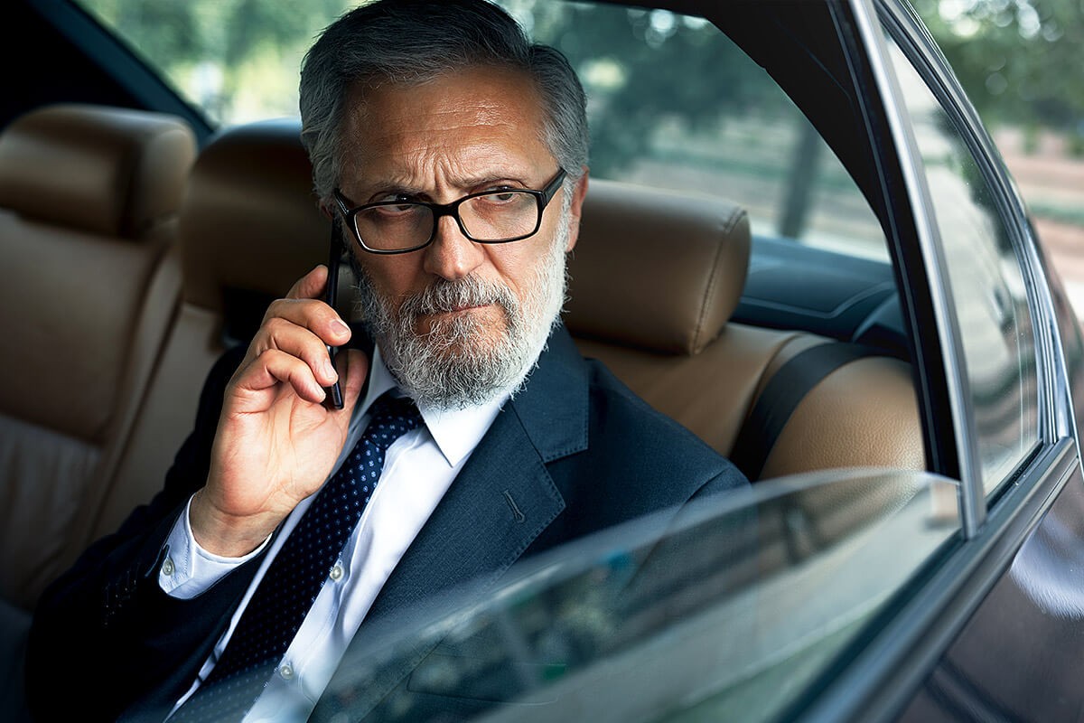 Wealthy man sitting in the back seat of a car and talking on a cell phone