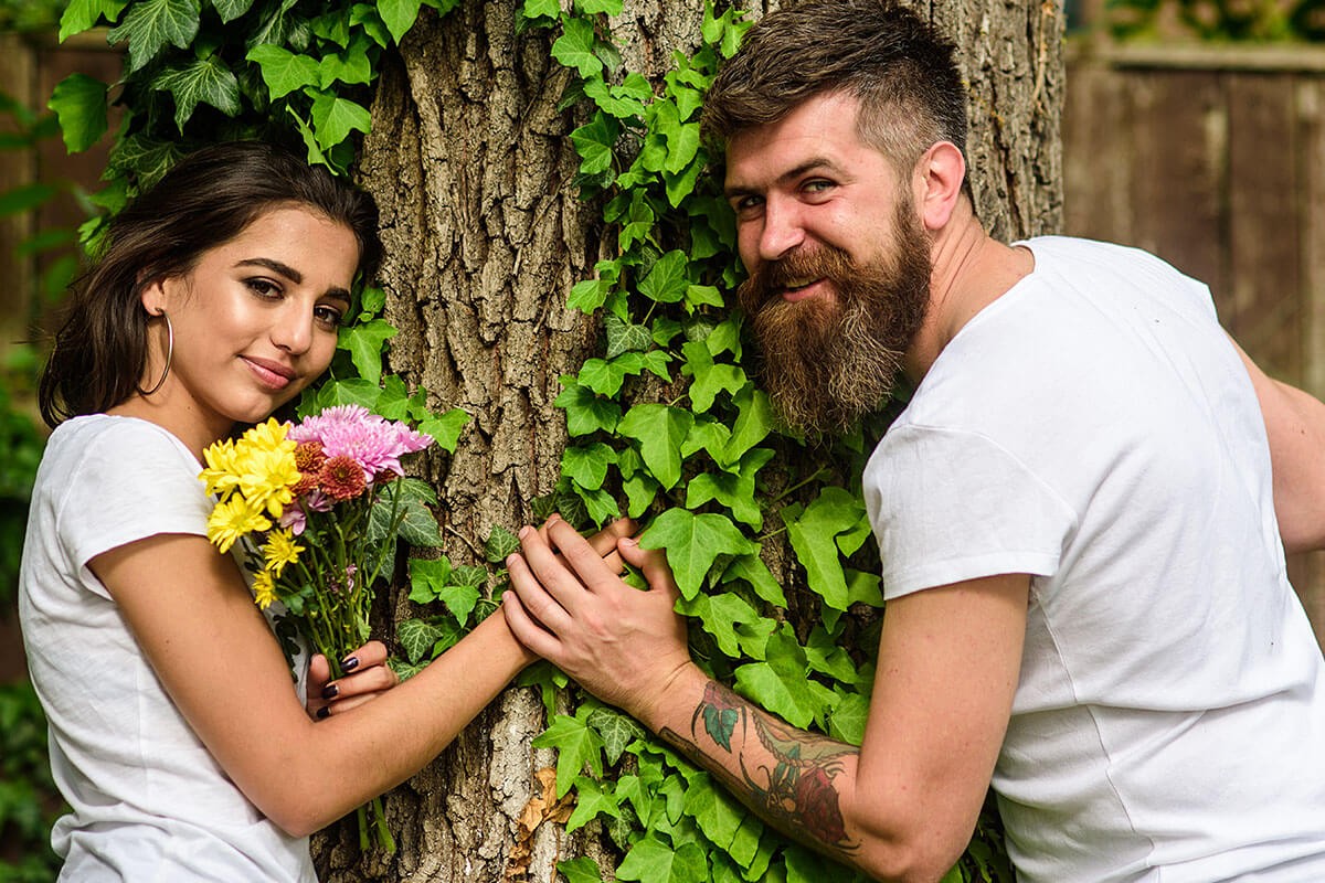 A man gives flowers to a woman by a tree