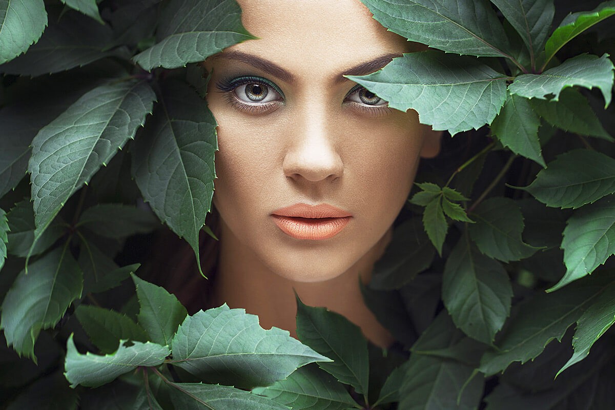 Female girl looks through the foliage
