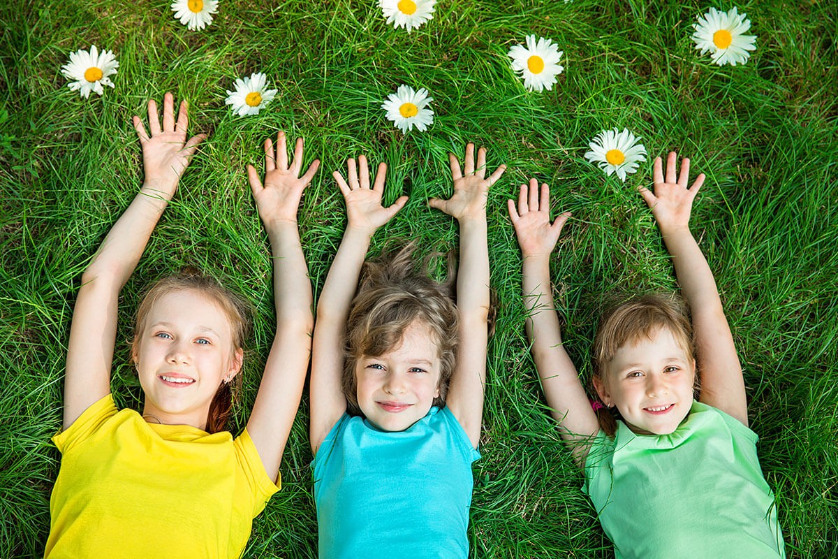 Joyful children lie on the grass with their hands up