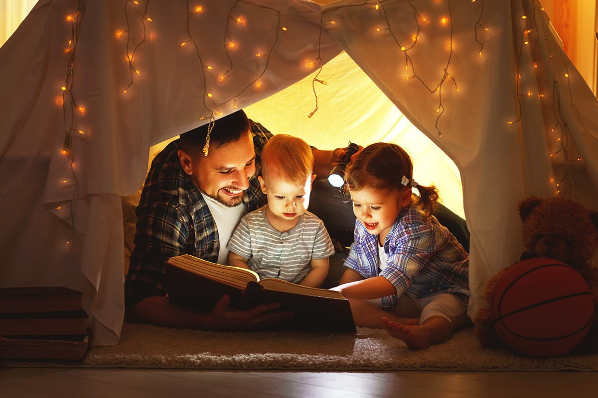 Dad with children in a small toy house reading a book