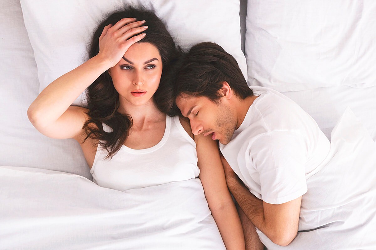 Displeased woman lies in bed with a sleeping man