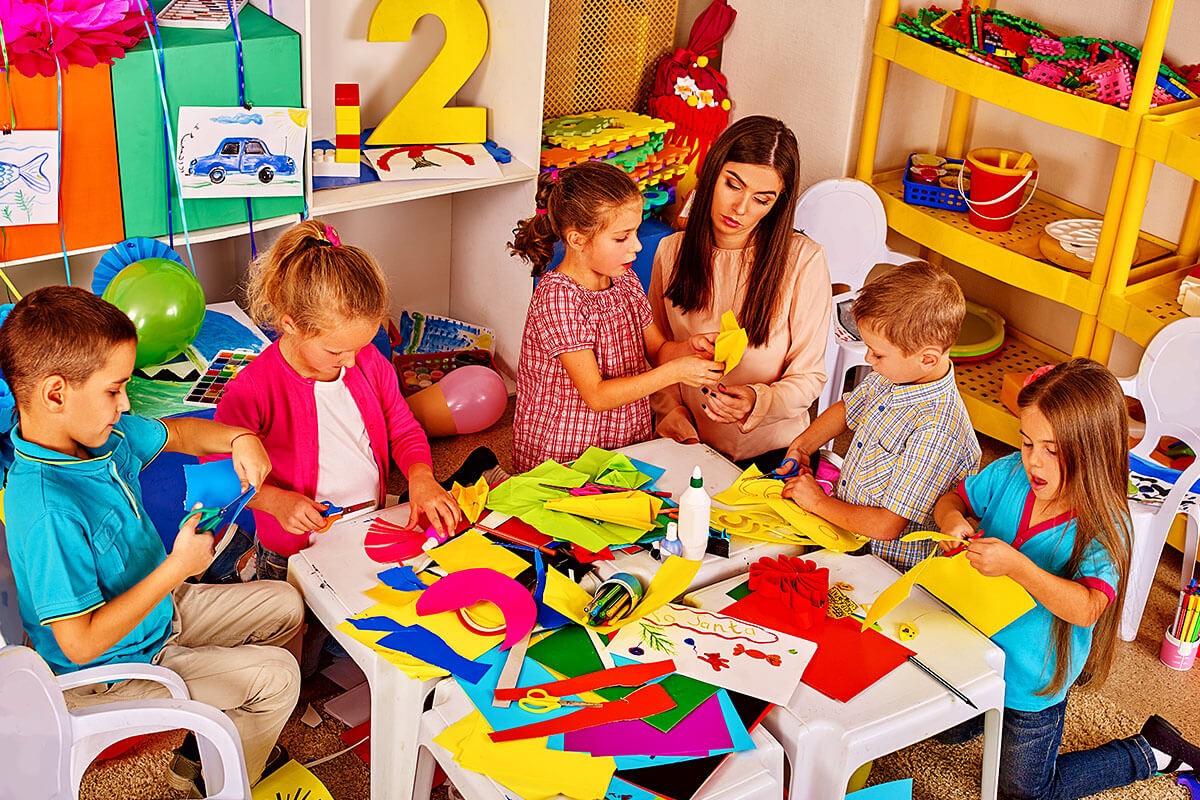 Preschool children are engaged in cutting figures out of paper with a teacher in the classroom