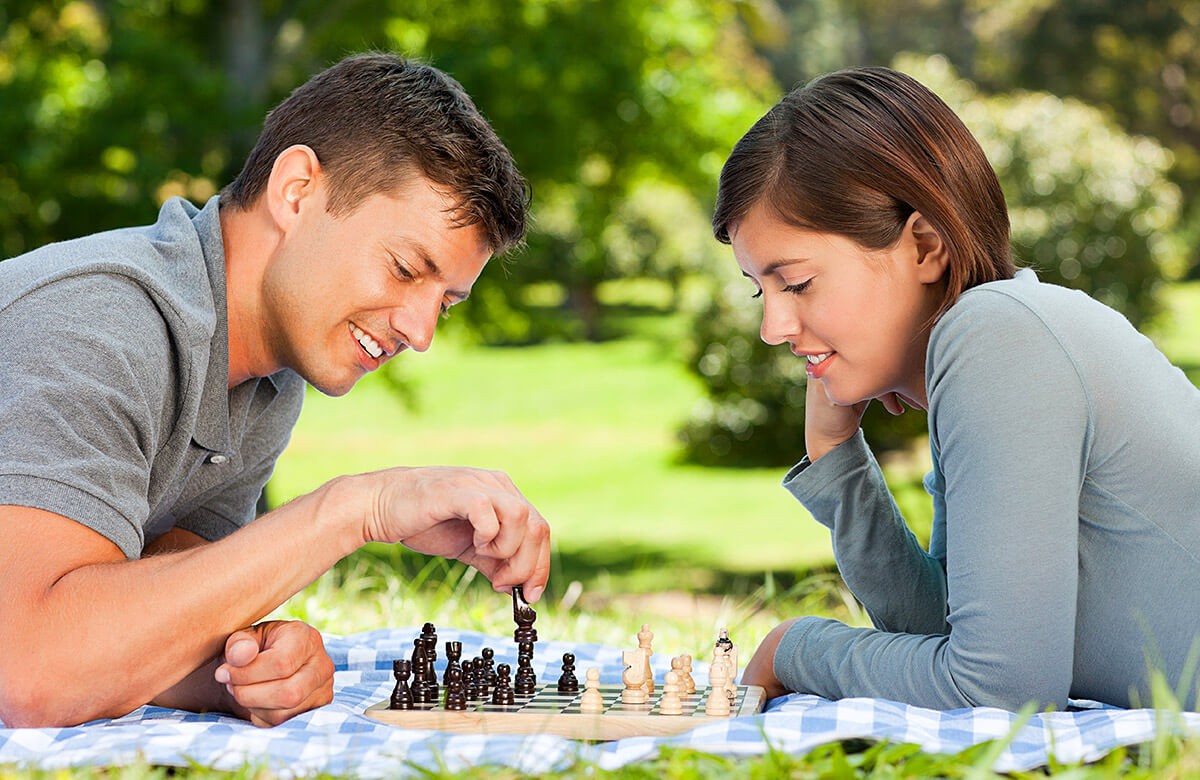 Young man plays chess lying on the grass with his girlfriend