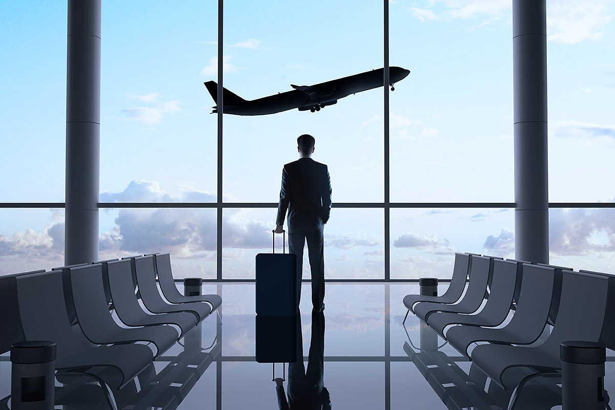 A man with a suitcase looks thoughtfully at a take-off plane