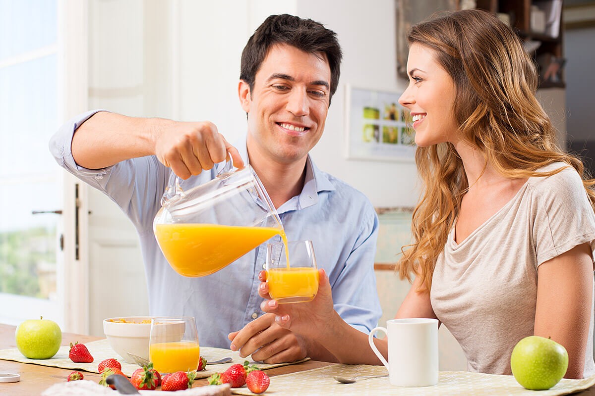 A man kindly pours juice for his woman