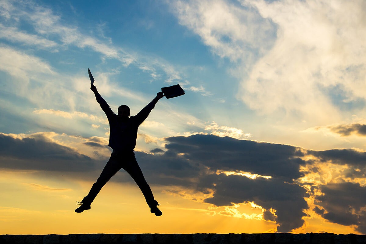 Businessman jumping with a briefcase in his hands at sunset
