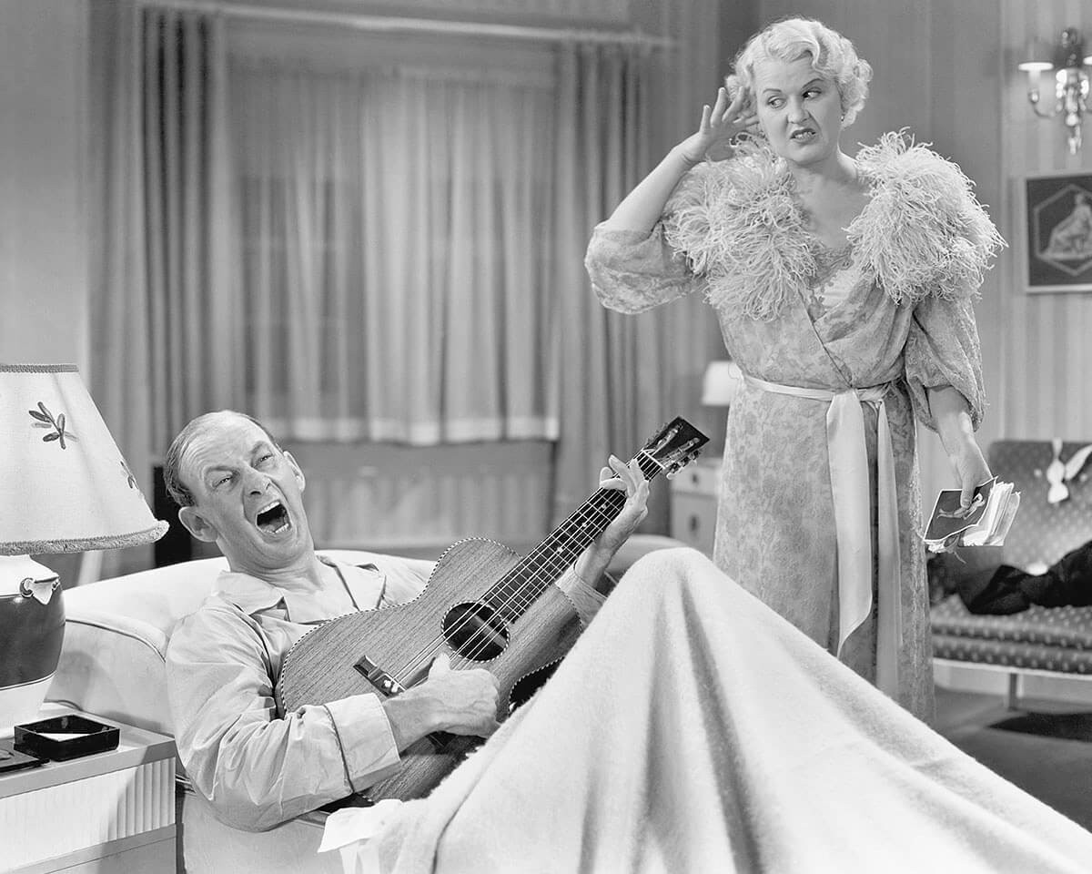 Image of a man playing a guitar and an amazed woman nearby