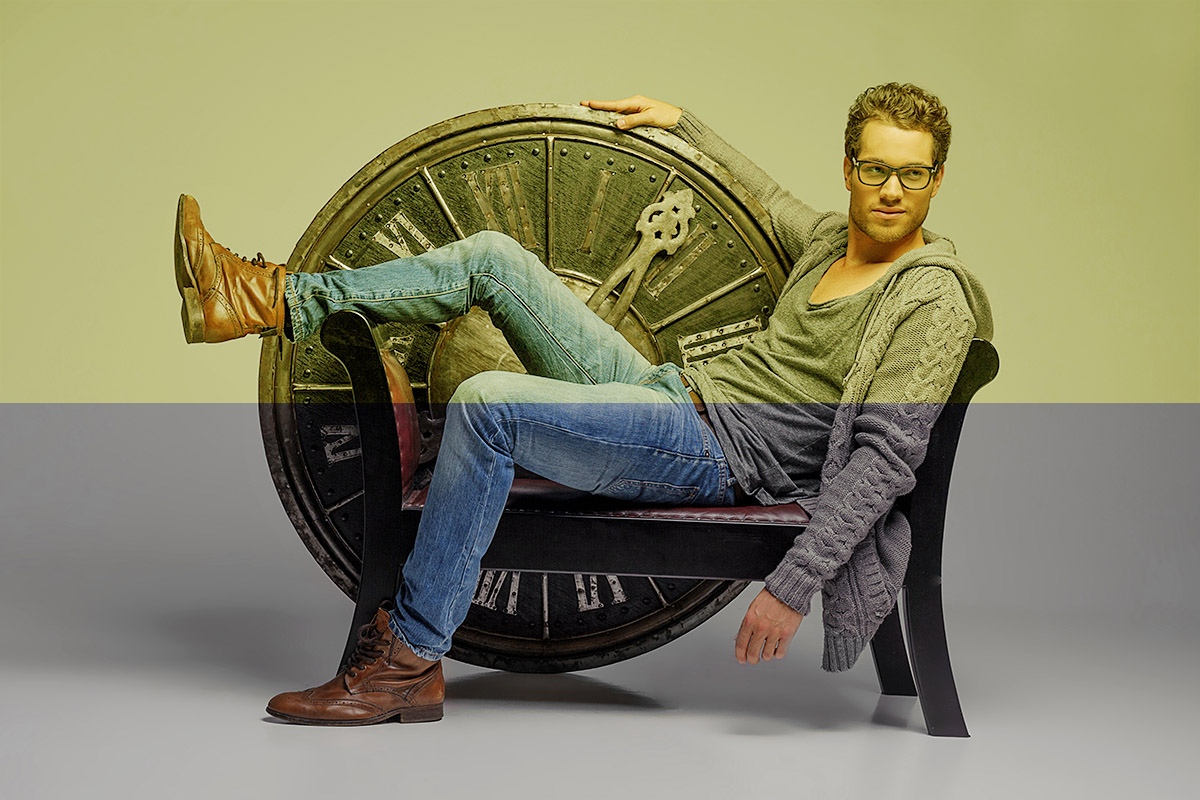 A young man sits with a large antique clock