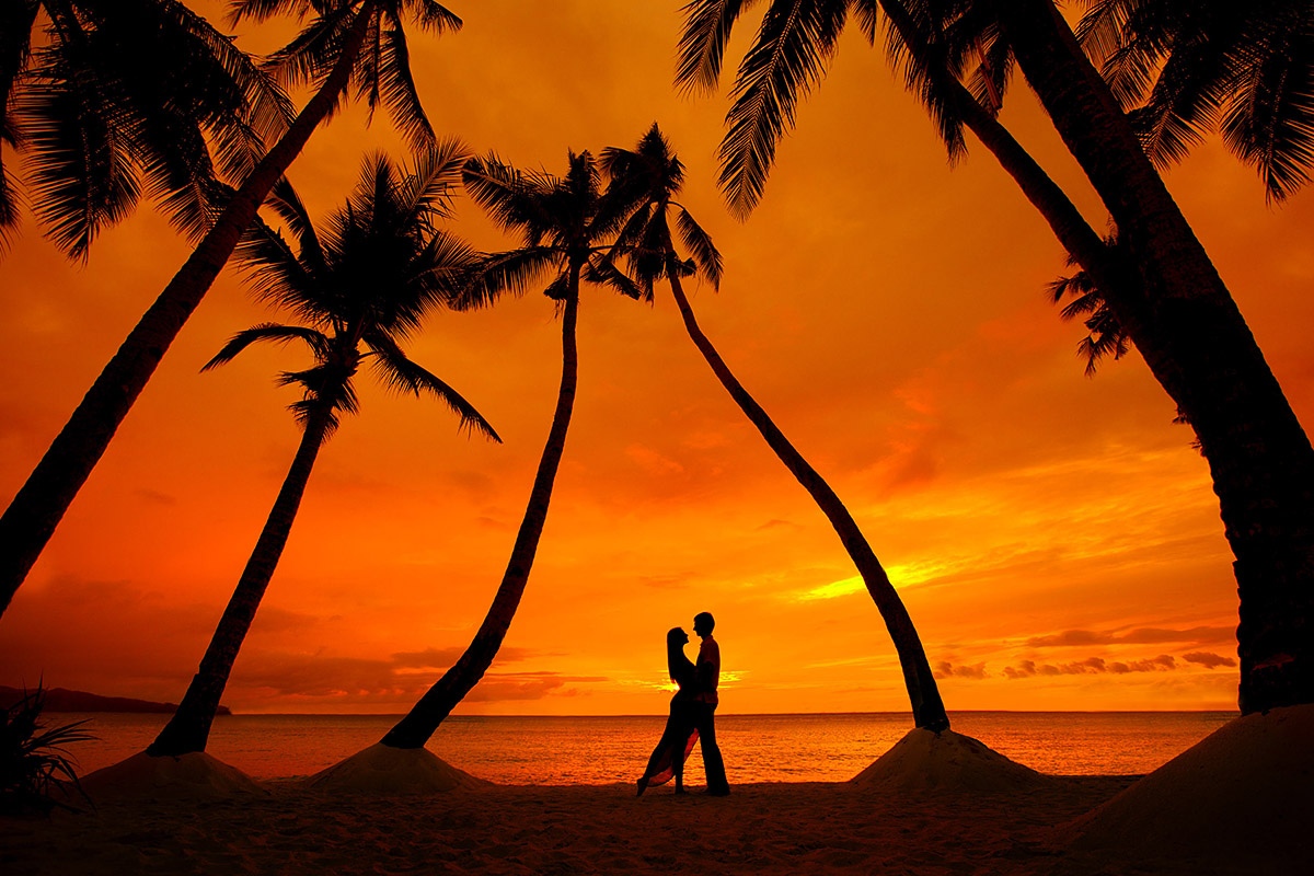 Image of a romantic couple on a tropical beach with palm trees at sunset time