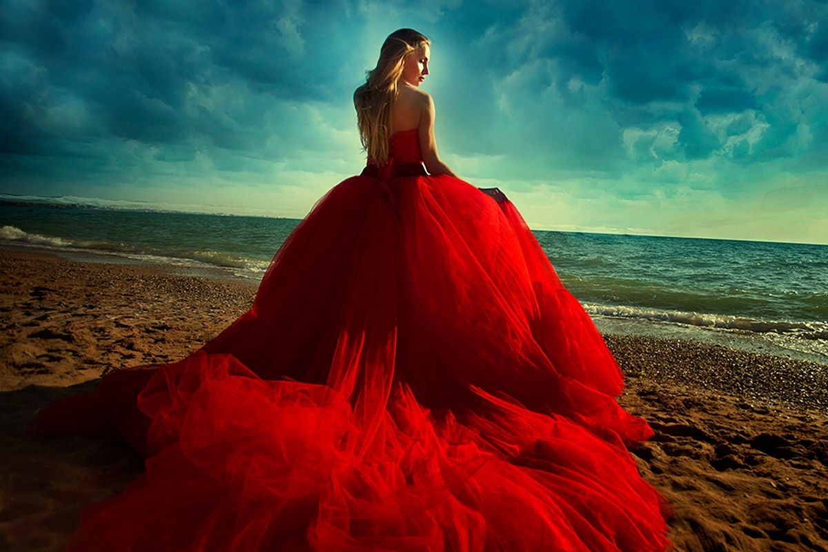 Photo of a girl in a lush red dress on the background of the coast