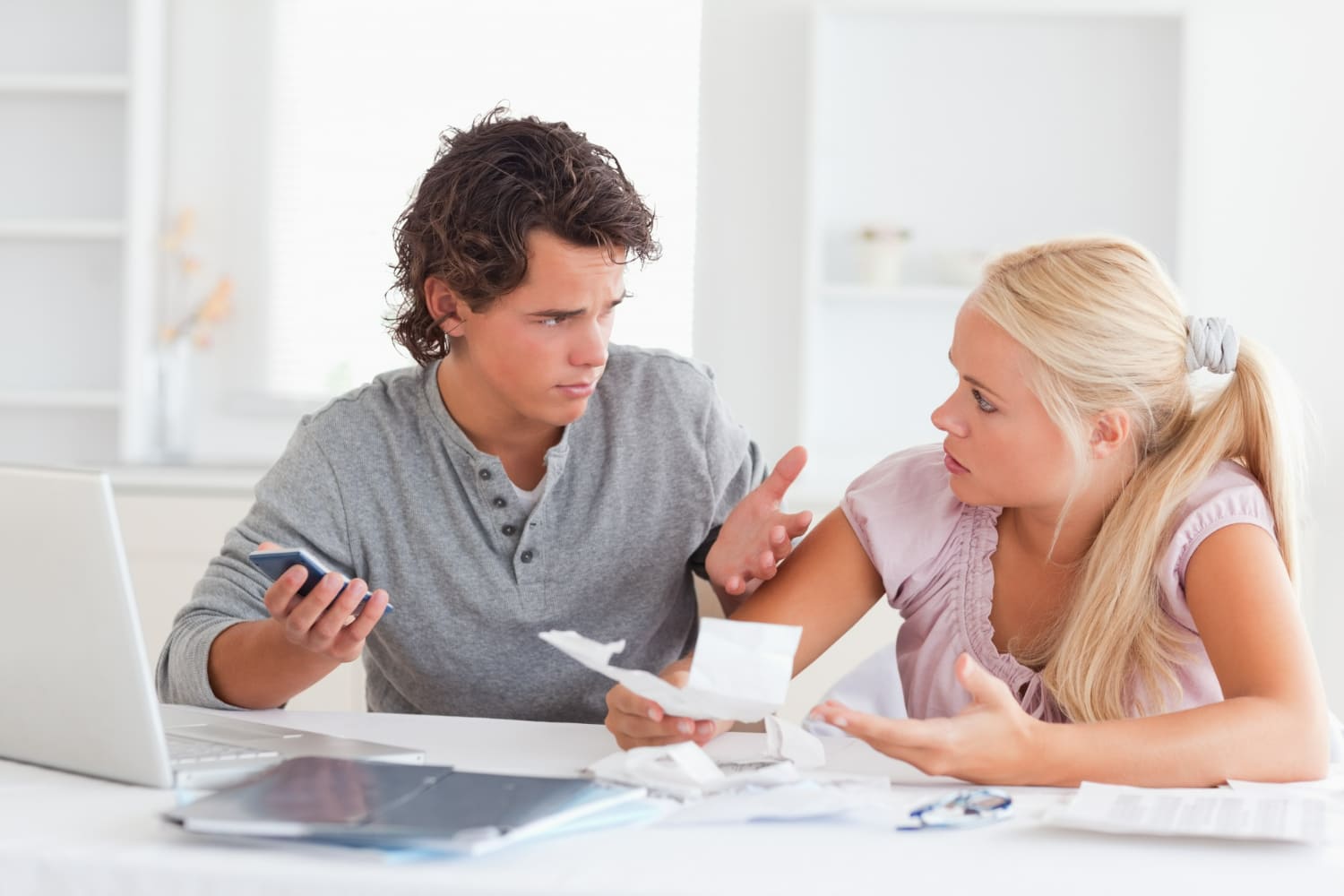 A young couple sitting at a table with bills and a smartphone, engaged in a tense discussion about finances, illustrating money problems, relationship conflict, budgeting stress, and financial disagreement. A young couple sitting at a table with bills and a smartphone, engaged in a tense discussion about finances, illustrating money problems, relationship conflict, budgeting stress, and financial disagreement.