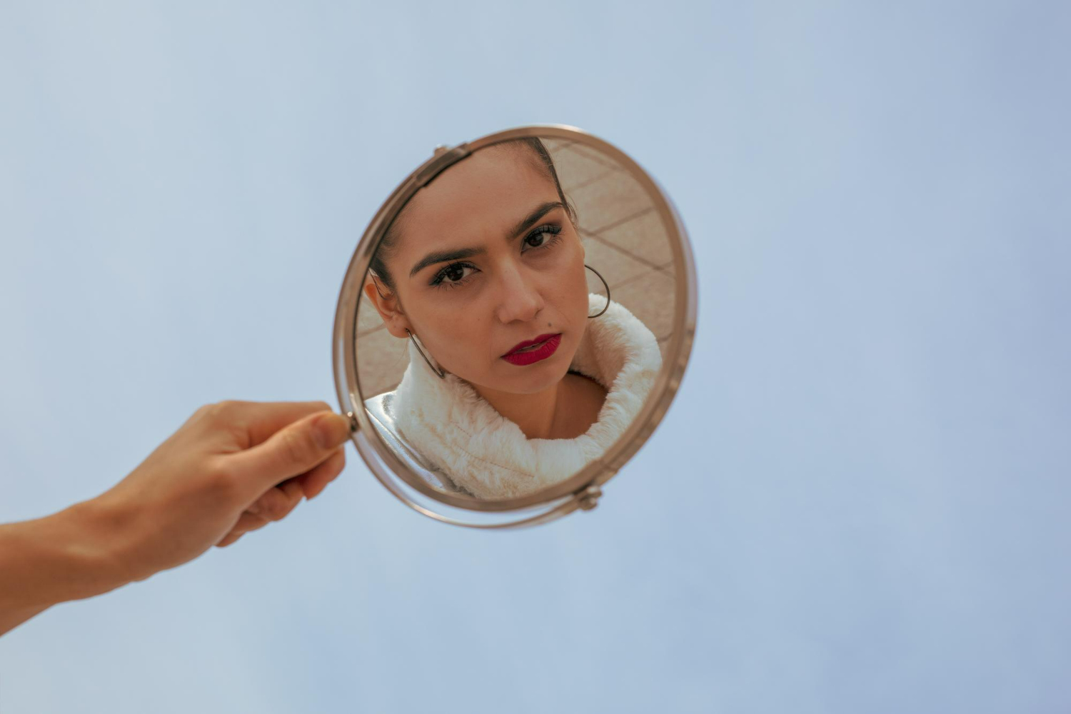 Portrait photography exploring identity and perception through the frame of a mirror, isolated against a soft blue backdrop.