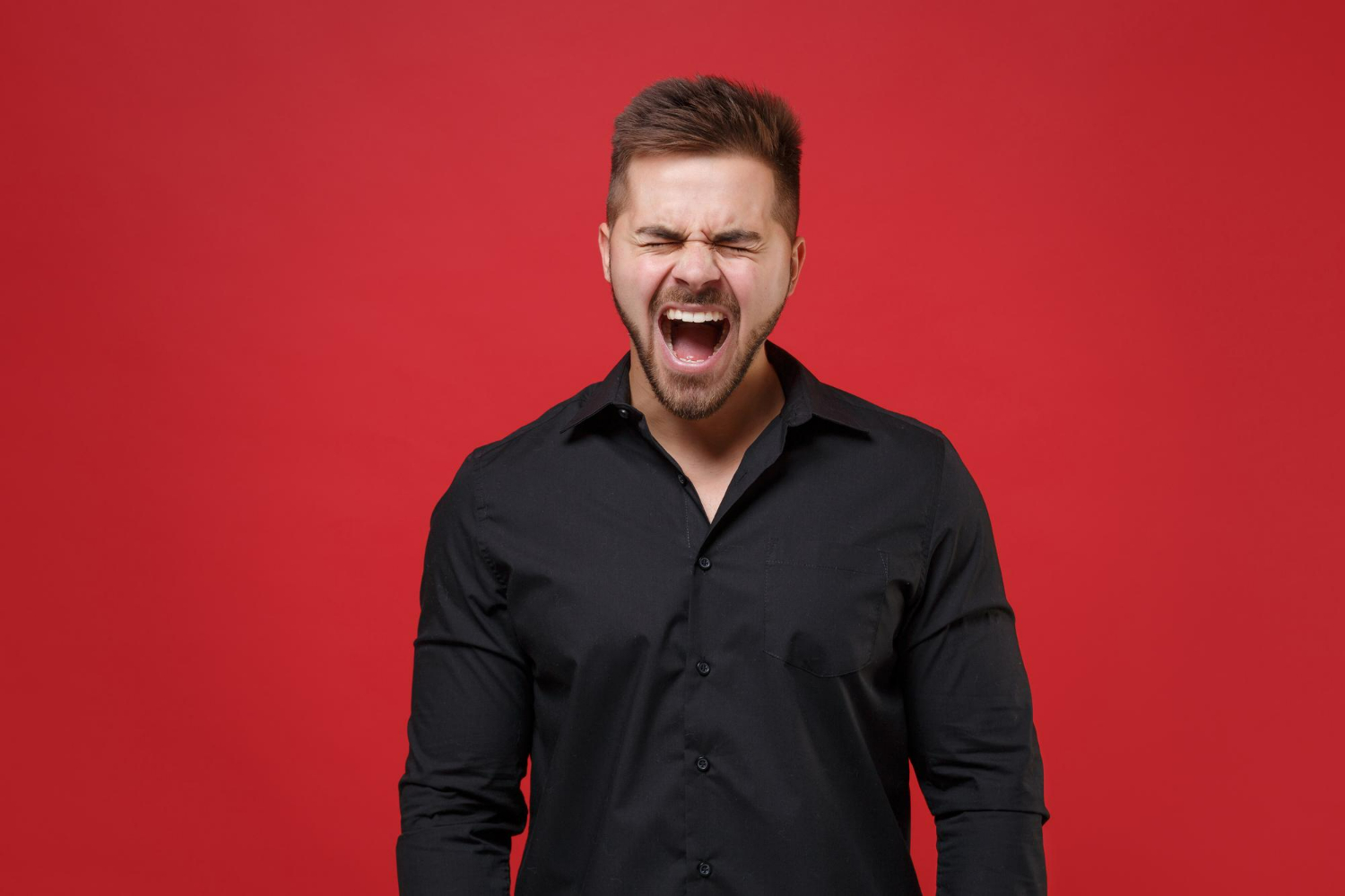 A young man screaming with his eyes closed against a bright red background, expressing intense emotion. A young man screaming with his eyes closed against a bright red background, expressing intense emotion.