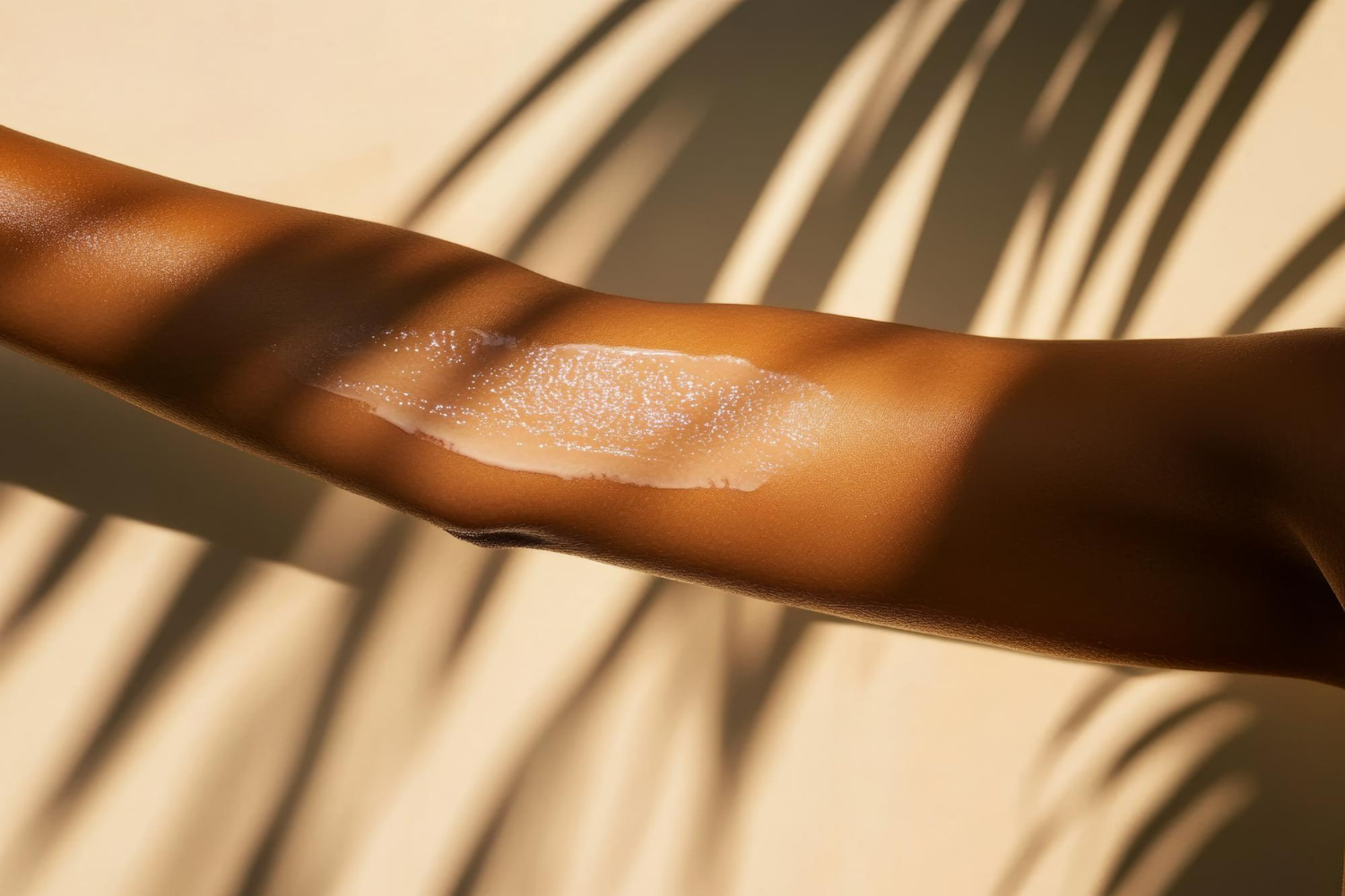 A close-up of a sun-kissed arm with a shimmering swipe of moisturizer or sunscreen applied, cast in warm golden light with dramatic palm leaf shadows across the skin. A close-up of a sun-kissed arm with a shimmering swipe of moisturizer or sunscreen applied, cast in warm golden light with dramatic palm leaf shadows across the skin.
