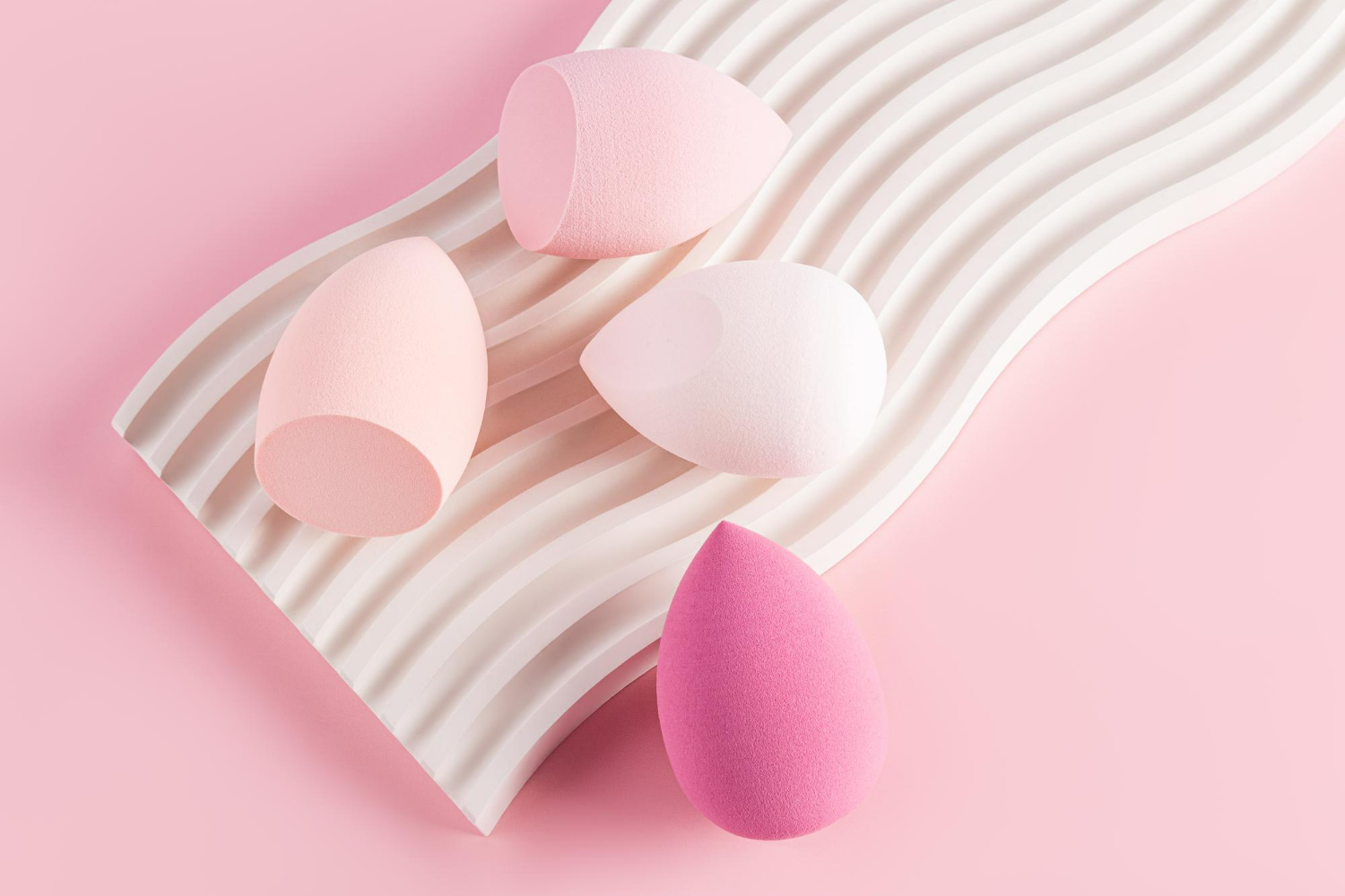 Four teardrop-shaped makeup blending sponges in shades of pink and white Four teardrop-shaped makeup blending sponges in shades of pink and white