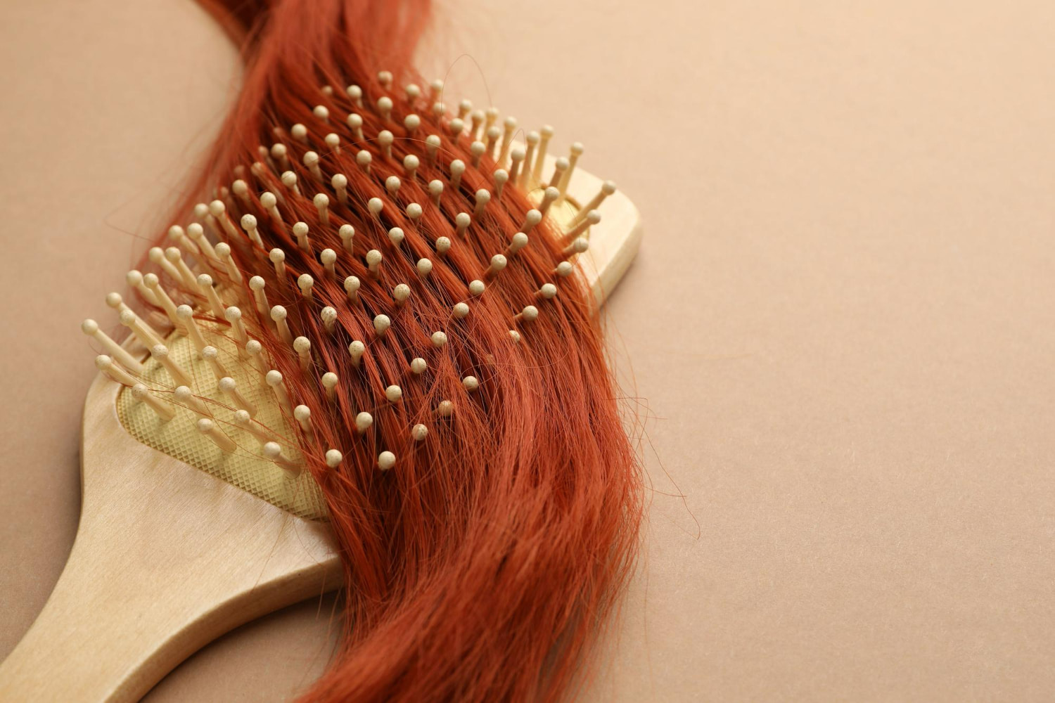 A close-up detail shot showcasing vibrant, copper-red hair being gently brushed with a natural wooden paddle brush.
