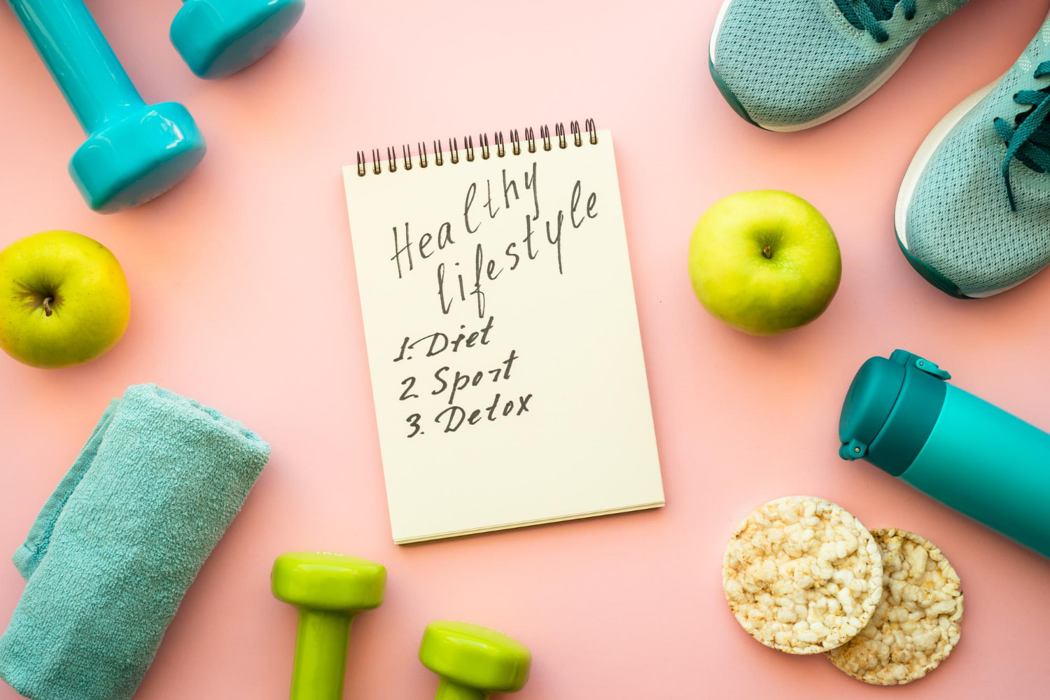 A flat lay composition on a pink background features a spiral notepad reading "Healthy lifestyle".