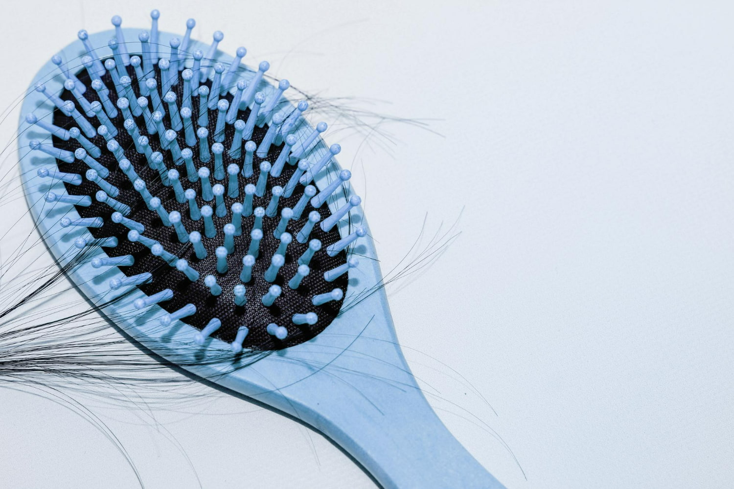 A professional product photography image showcasing a modern blue hair brush with innovative ball-tipped bristles against a clean, minimalist white background.