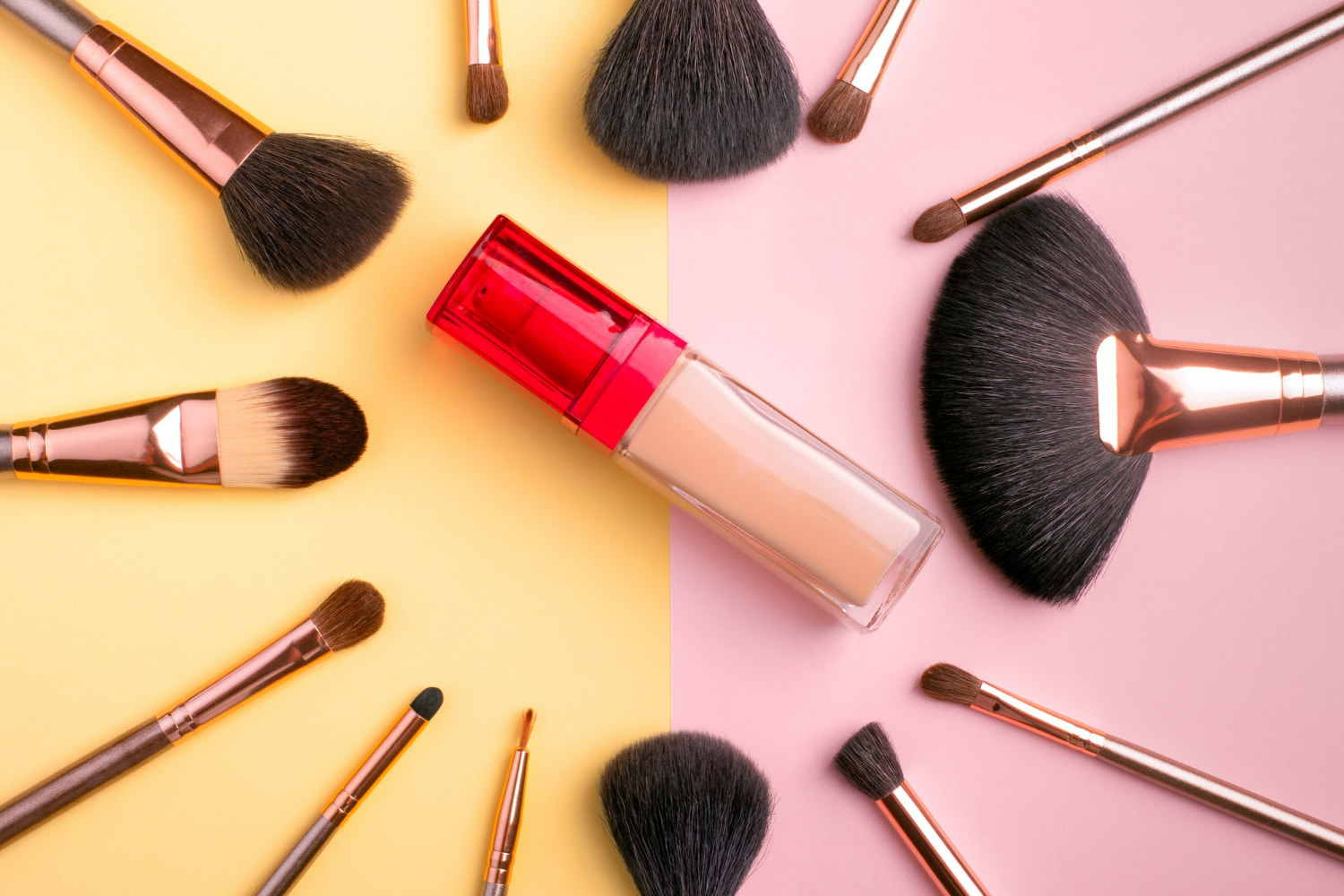 Set against a bold split background of soft yellow and pastel pink, the image showcases essential beauty tools and products in perfect symmetry.