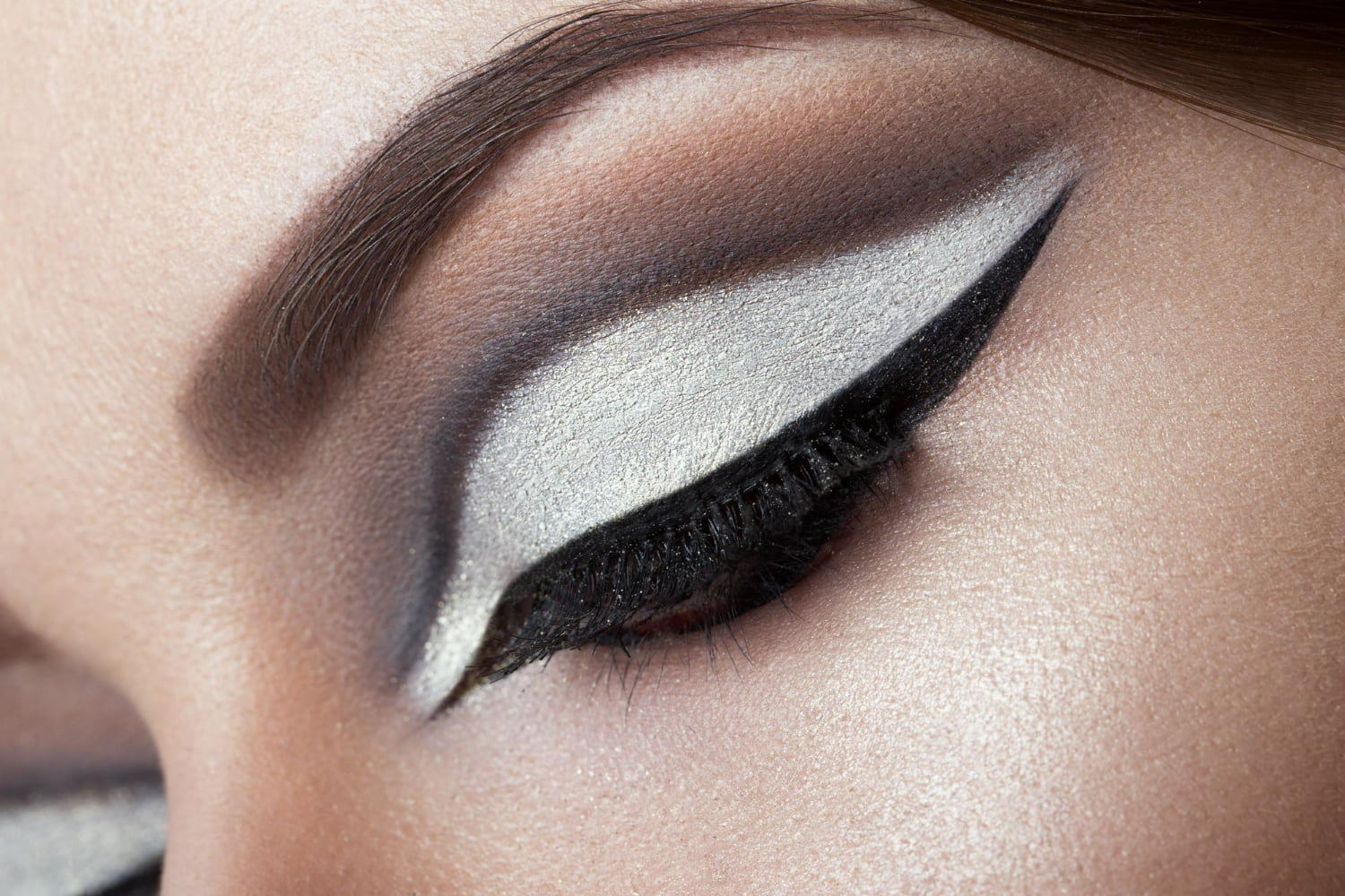 A sophisticated close-up of expertly-applied eyeshadow and eyeliner showcasing a classic smokey eye look with modern metallic accents.
