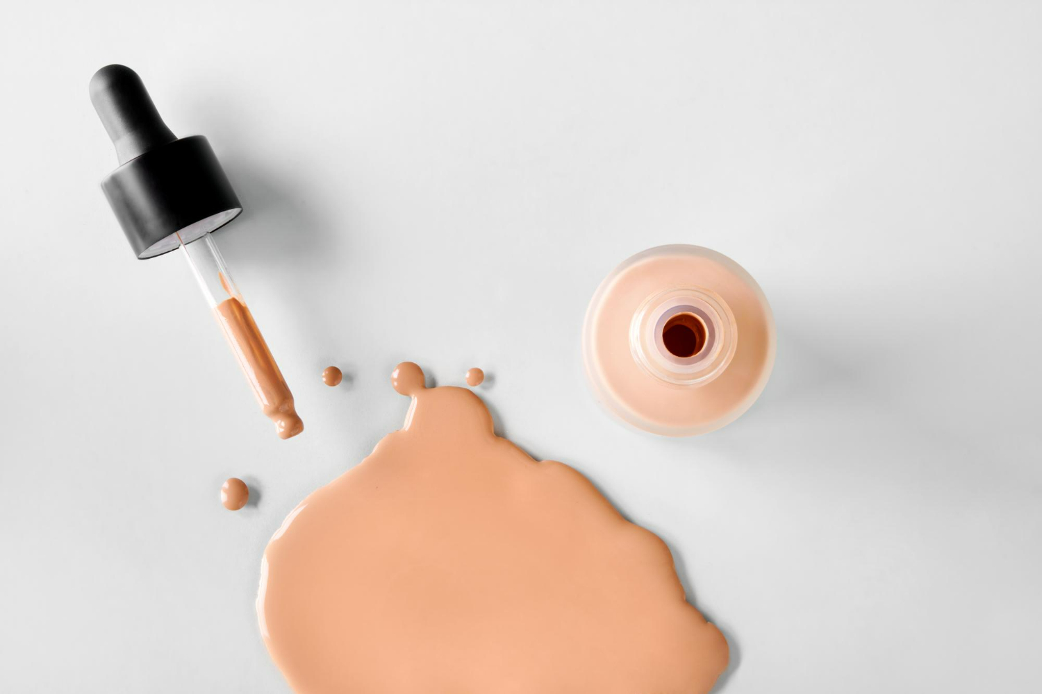 A professional flat lay of liquid foundation product featuring a dropper bottle with black cap and wooden applicator.