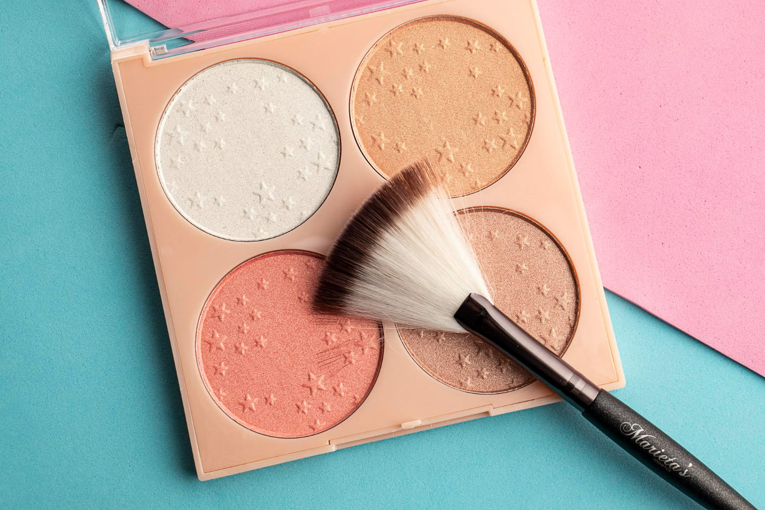A luxurious makeup brush with soft white bristles and a black handle rests artfully on the palette, ready for application.